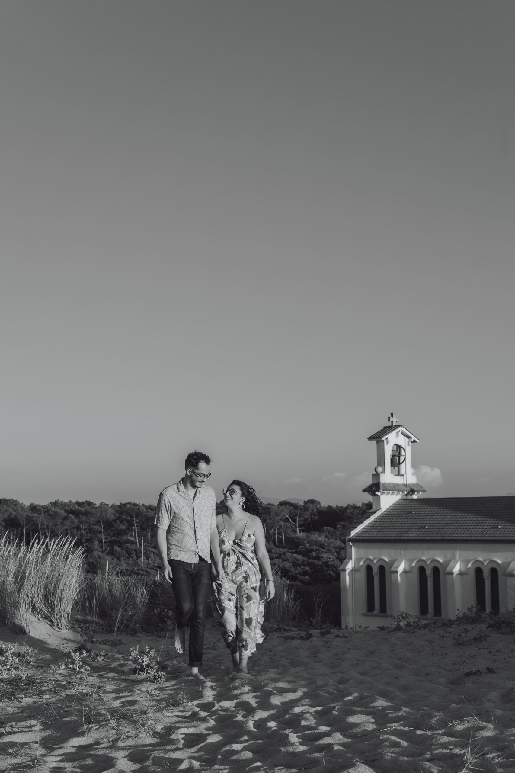 Séance photo noir e blanc d’un couple sur la plage de Labenne, complicité et tendresse au coucher du soleil devant la chapelle.