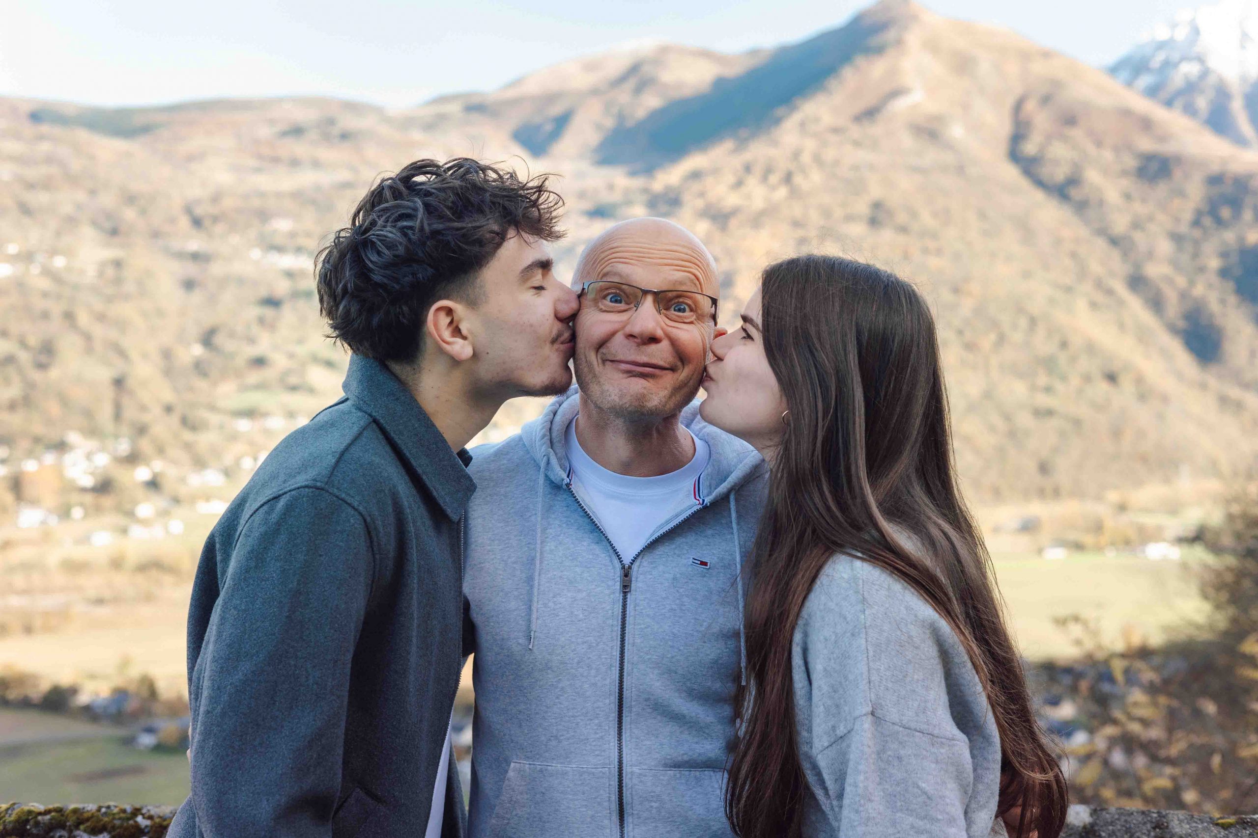 photographe famille argeles gazost Deux ados embrassant leur père sur les joues pendant une séance photo famille en extérieur