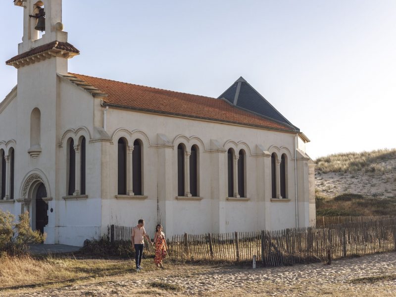 Couple profitant d’une séance d’engagement romantique sur la plage de Labenne avec la chapelle en arrière-plan au coucher du soleil. sandrine afonso photographe mariage sud ouest